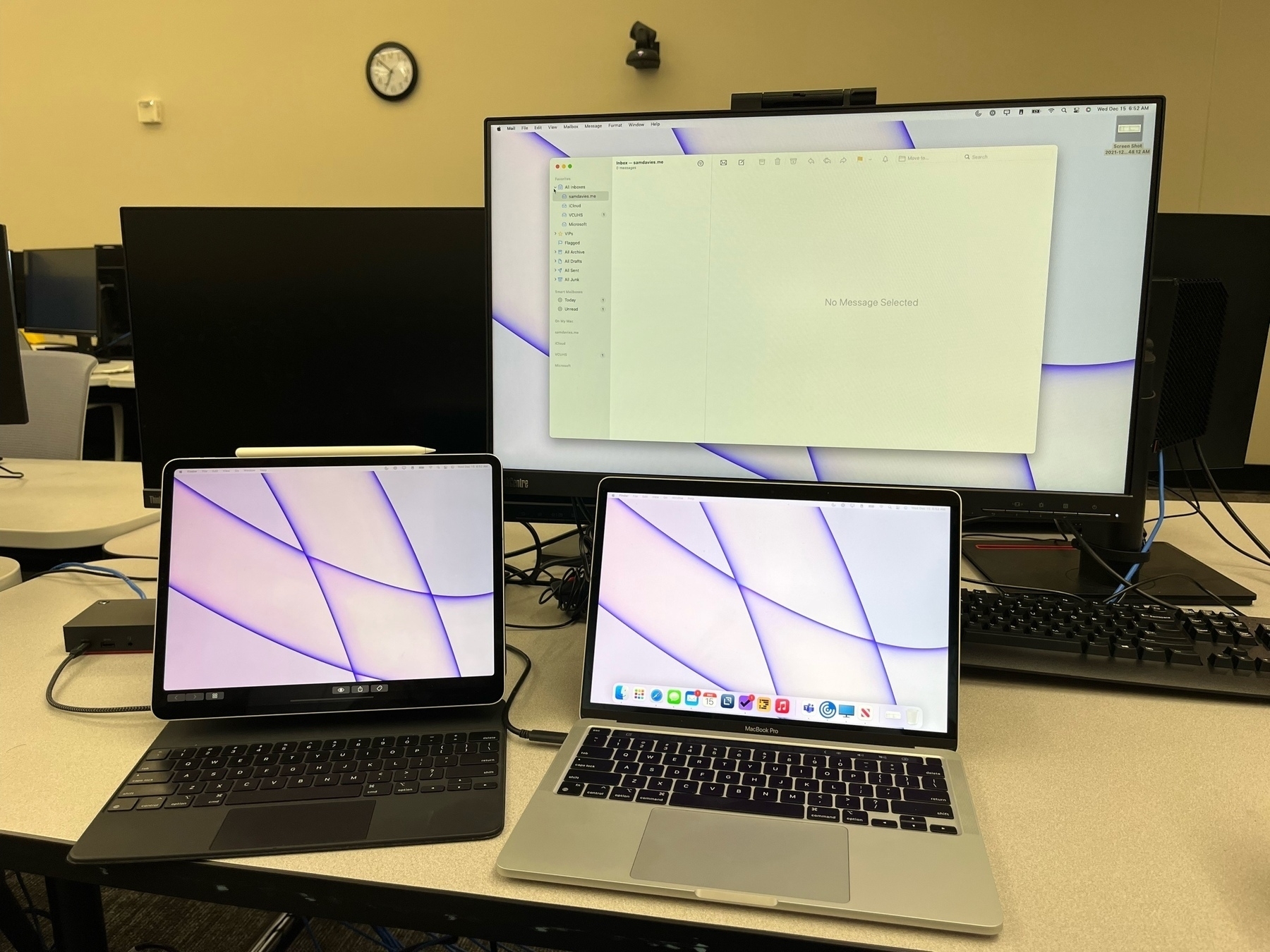 A 12.9" iPad Pro shows the macOS desktop alongside a MacBook Pro and ThinkCentre monitor